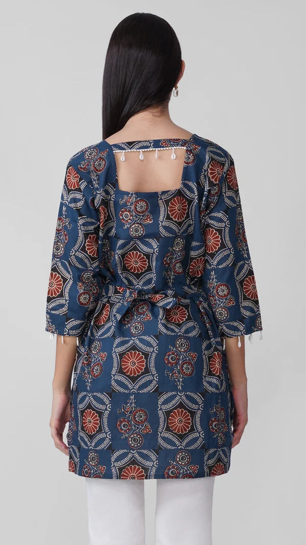 Young woman wearing a navy blue printed kurta top with rust floral and paisley motifs, three-quarter sleeves, pearl-trim cuffs and white trousers.