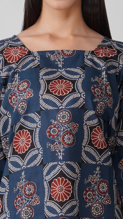 Young woman wearing a navy blue printed kurta top with rust floral and paisley motifs, three-quarter sleeves, pearl-trim cuffs and white trousers.