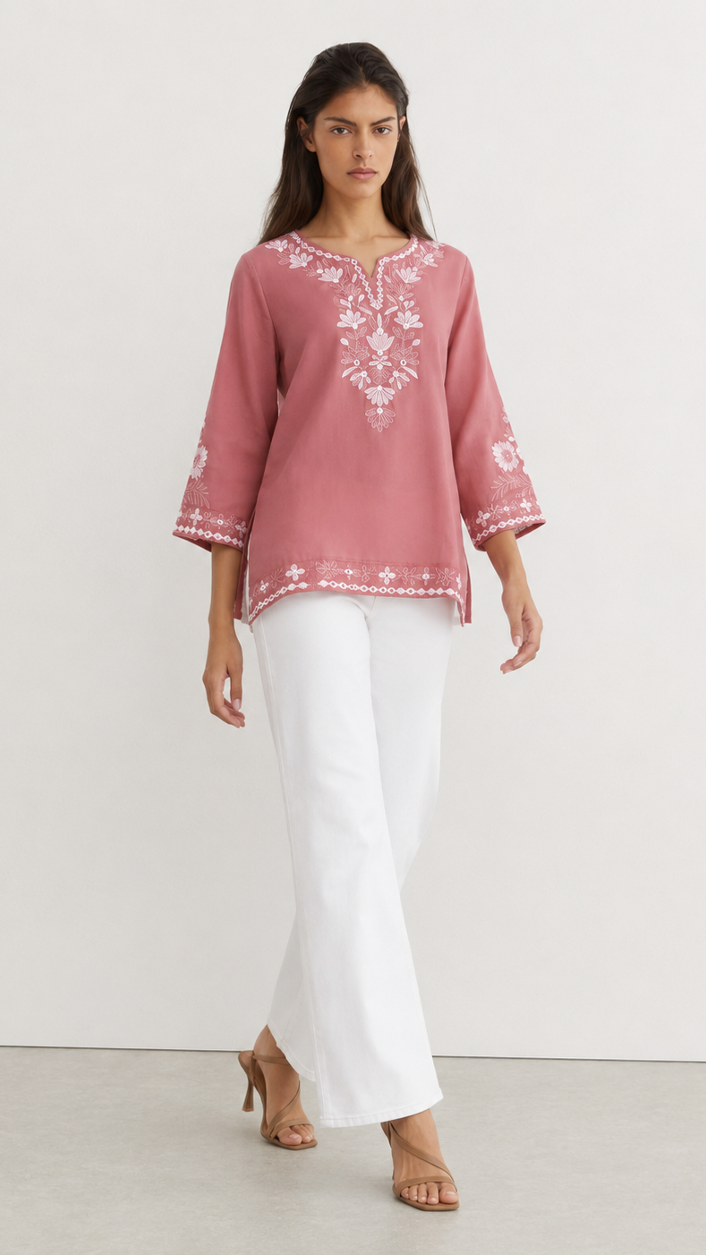 Young woman wearing a dusty rose embroidered kurta top with white floral threadwork, three-quarter sleeves and white flared trousers.