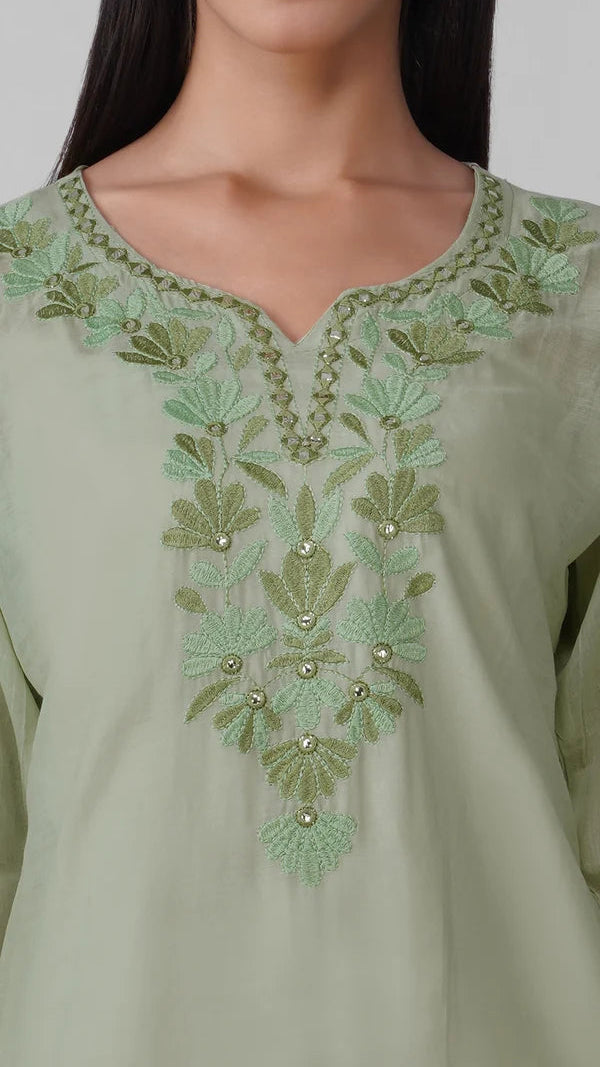 Young woman wearing a sage green embroidered kurta top with tonal floral threadwork, three-quarter sleeves and white trousers.