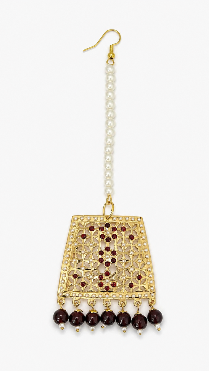 A single gold-toned dangle earring with a vertical strand of white faux pearls, a rectangular filigree gold pendant decorated with small red stones.