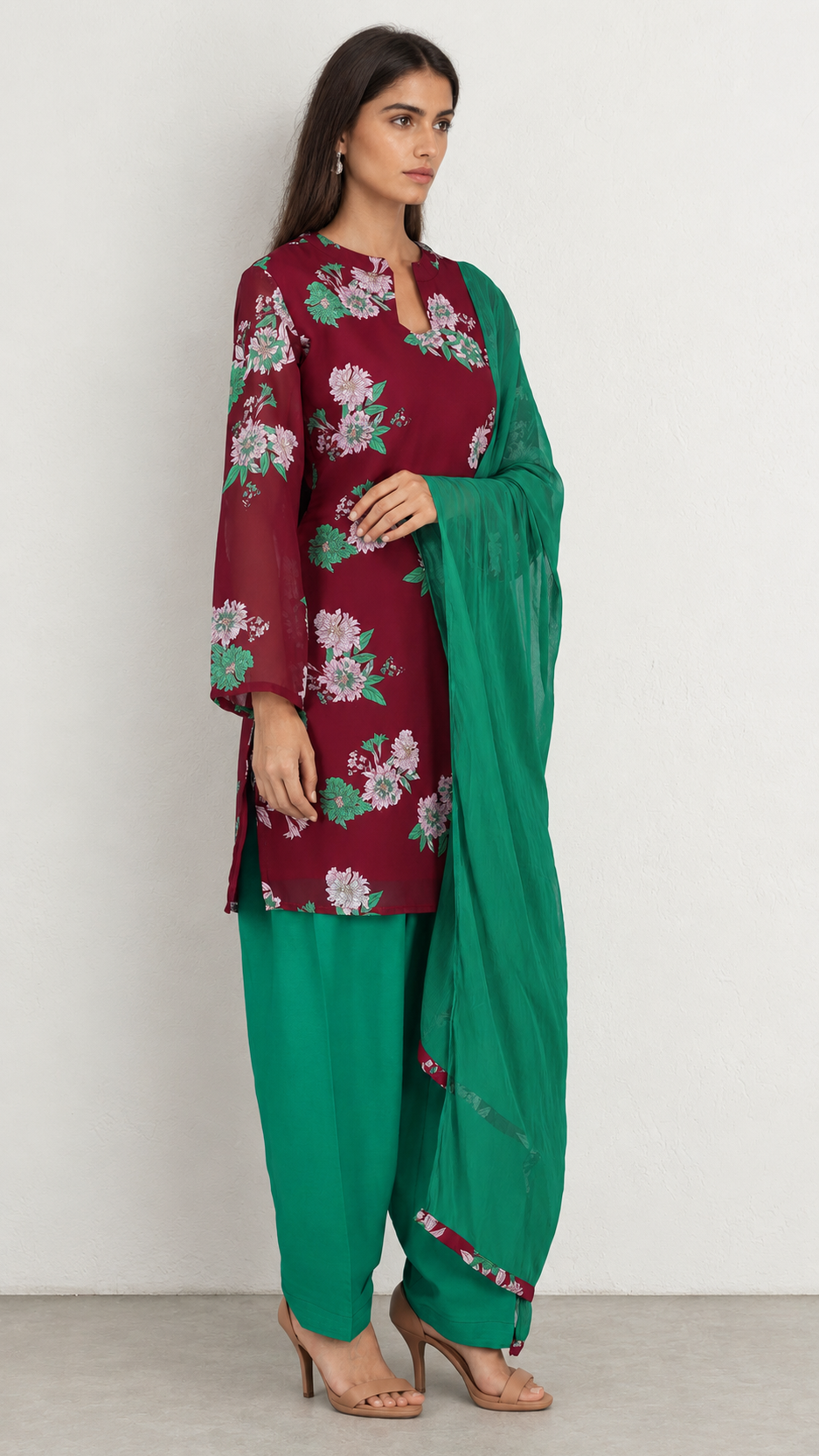 A woman modeling a traditional Indian salwar kameez suit. The outfit features a deep maroon kameez jacket with white and green floral embroidery, paired with solid green pants and a matching green dupatta.