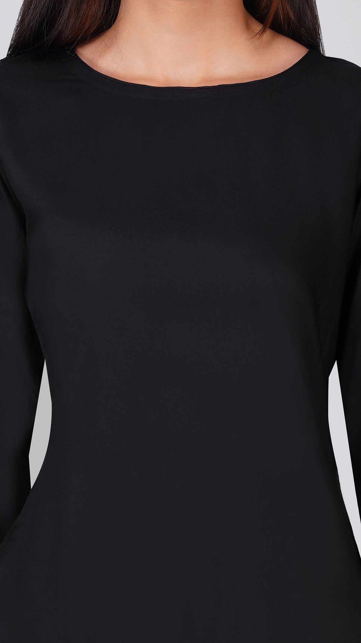 A close-up of a woman wearing a solid black long-sleeve top with a wide boat neckline, shown against a light gray background.