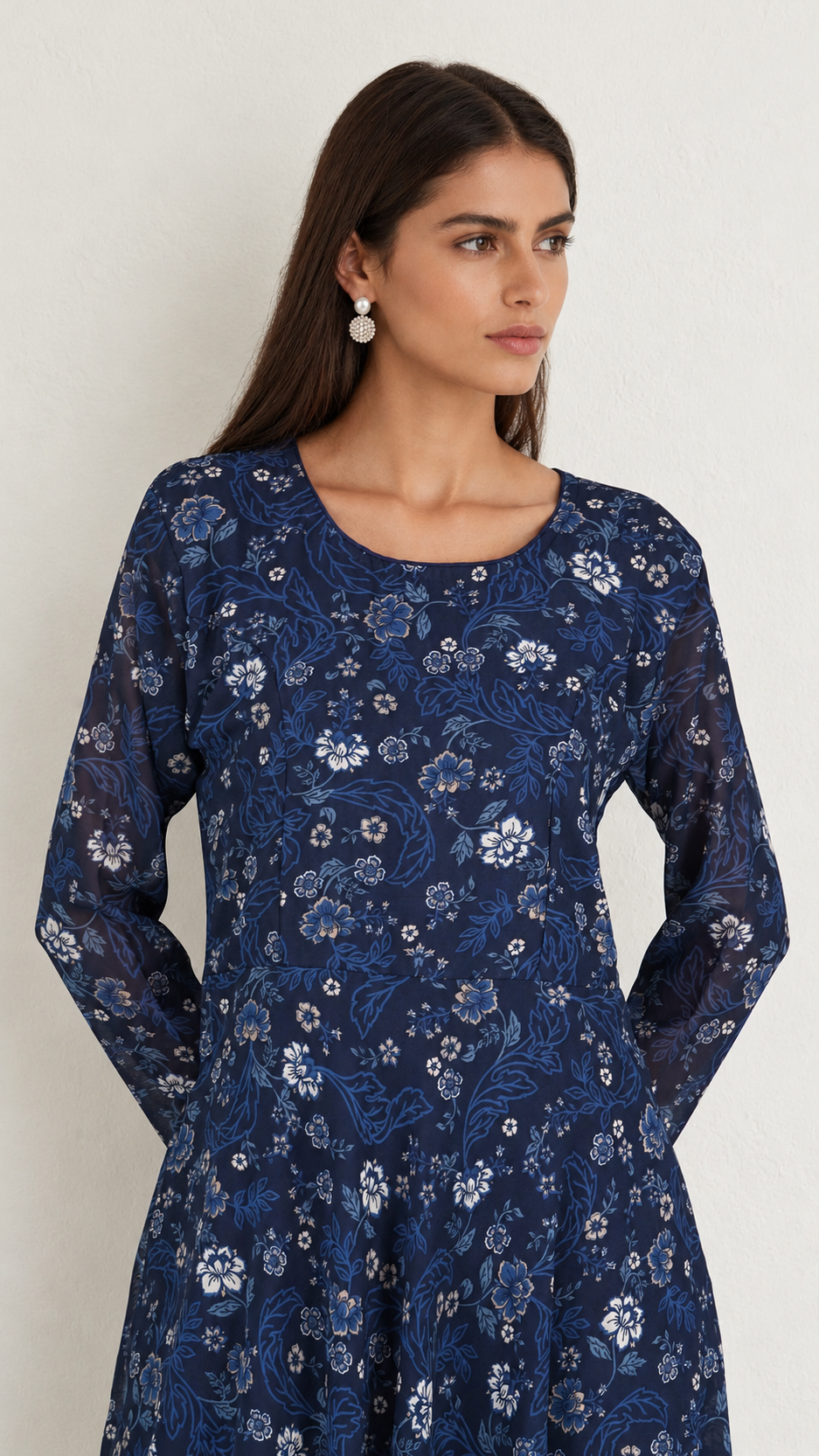 A woman wearing a long-sleeve navy blue tunic dress with a white floral pattern, photographed against a plain light background.
