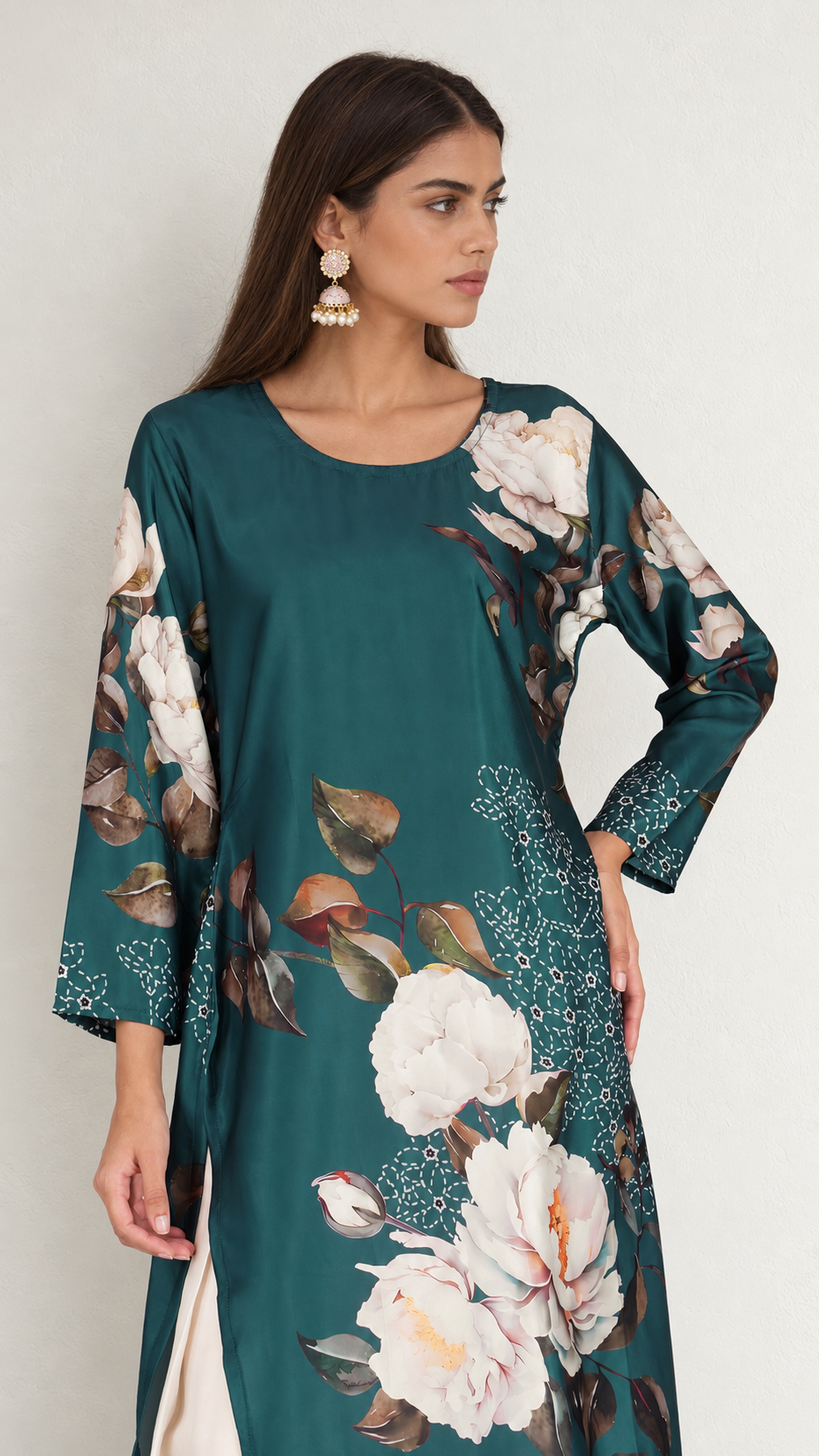 A woman wearing a teal green long-sleeve tunic dress with a large white and pink floral print, photographed against a light gray studio background.