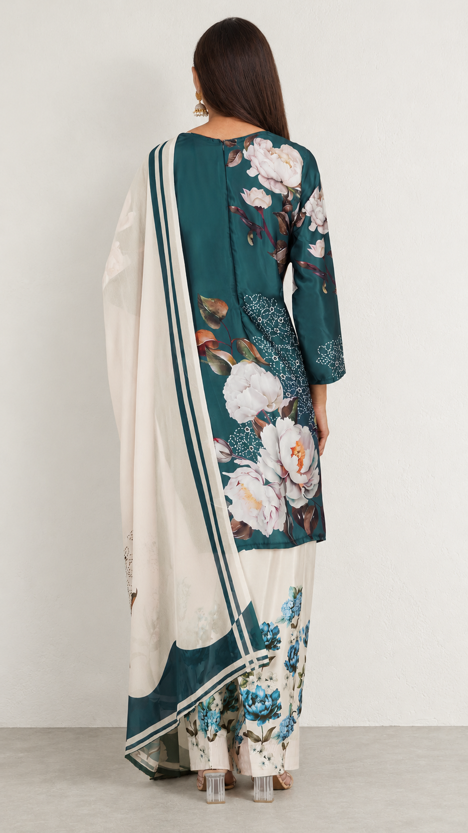 A woman shown from the back wearing a traditional three-piece salwar kameez outfit. The outfit features a dark teal green tunic with a large white and pink floral print, matching printed trousers, and a cream-colored dupatta with teal borders.
