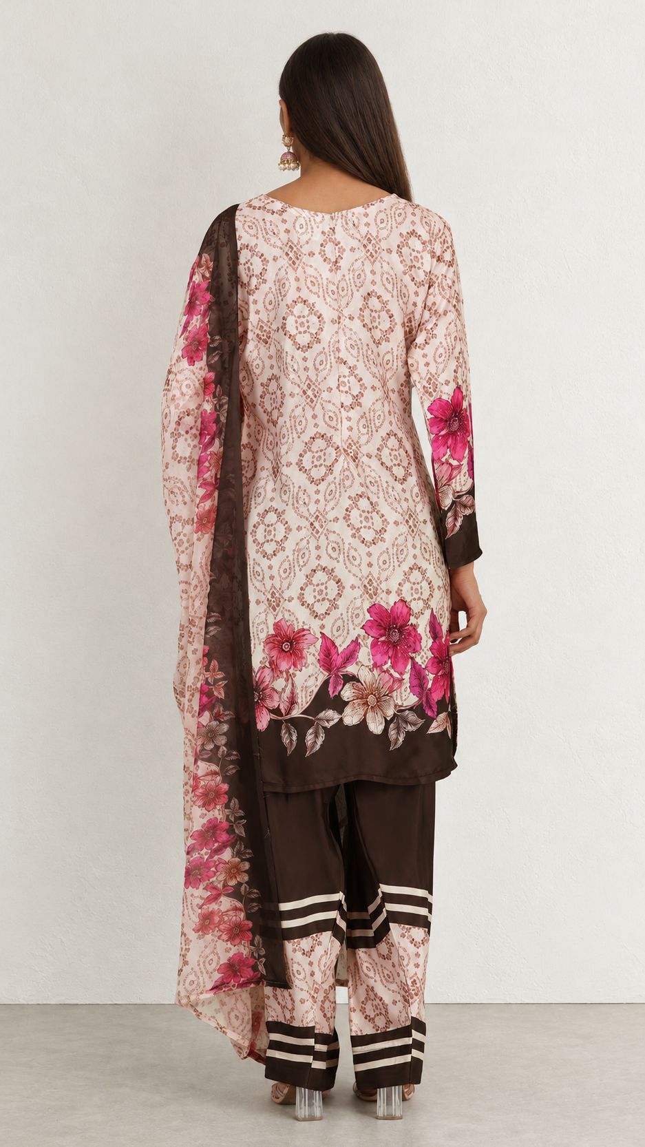 A woman shown from the back wearing a traditional three-piece salwar kameez suit. The set features a light pink and beige floral printed kurta with dark brown borders and pink floral embroidery, paired with matching brown trousers and a dark brown dupatta.