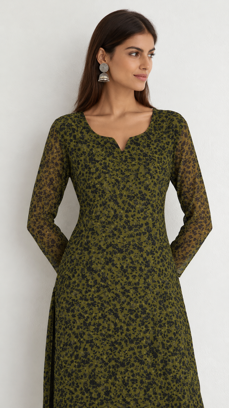 A woman wearing a long-sleeved olive green kurta with a black abstract animal print pattern, standing against a plain light gray wall.