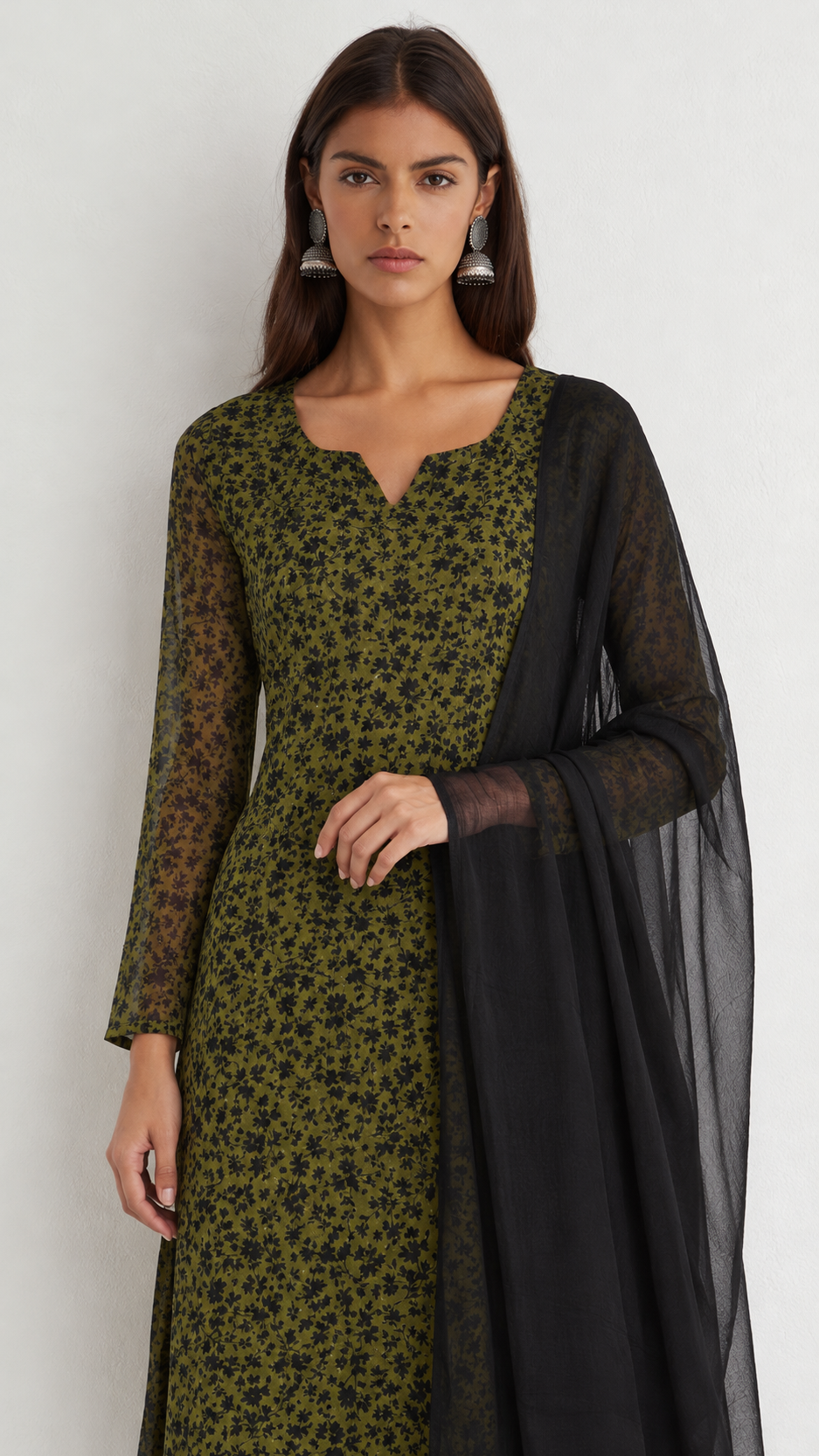A woman modeling a green and black patterned kurta with sheer black sleeves and a matching black dupatta, photographed against a plain light gray background.