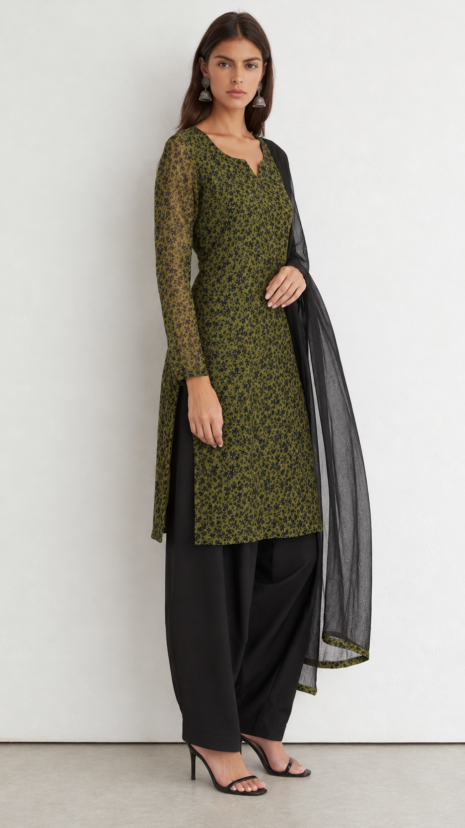 A woman modeling a green and black patterned kurta with black wide-leg pants and a sheer black dupatta, standing against a plain light gray wall.