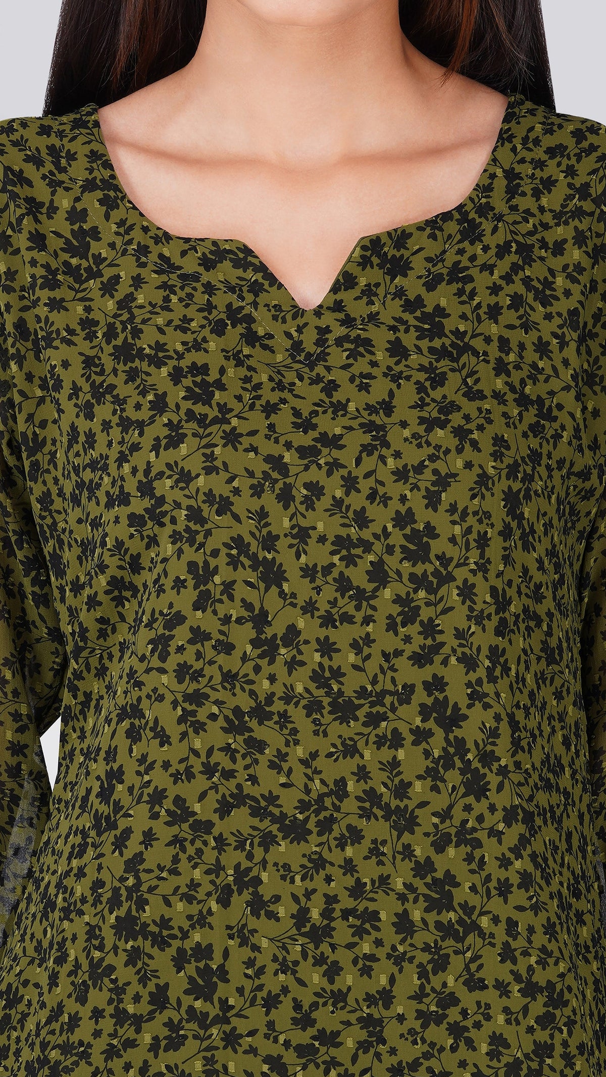 A close-up of a woman wearing a long-sleeve olive green top with a black floral print and a split V-neckline.