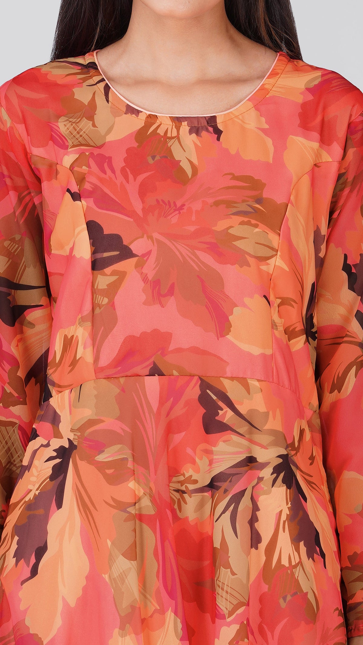 A close-up of a model wearing a long-sleeve top with a vibrant floral pattern in shades of orange, pink, and brown.