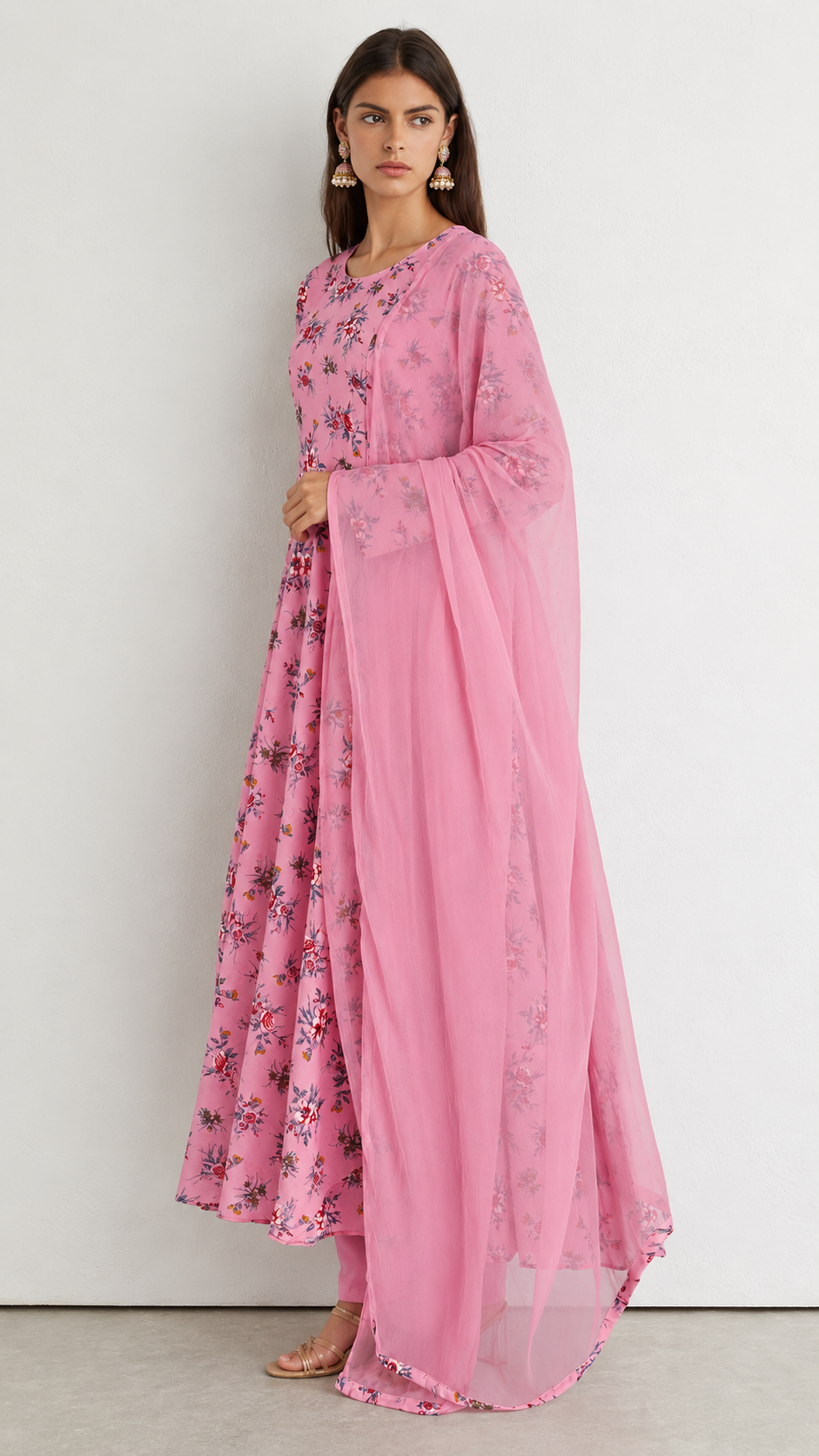 A woman models a pink floral printed anarkali suit with a matching sheer pink dupatta against a plain white studio background.