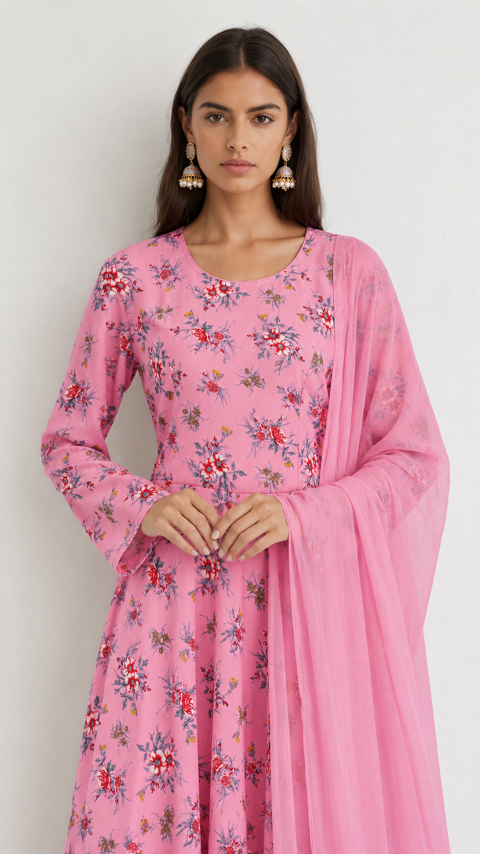 A woman modeling a pink floral printed kurta with long sleeves and a matching sheer pink dupatta, set against a plain light gray background.