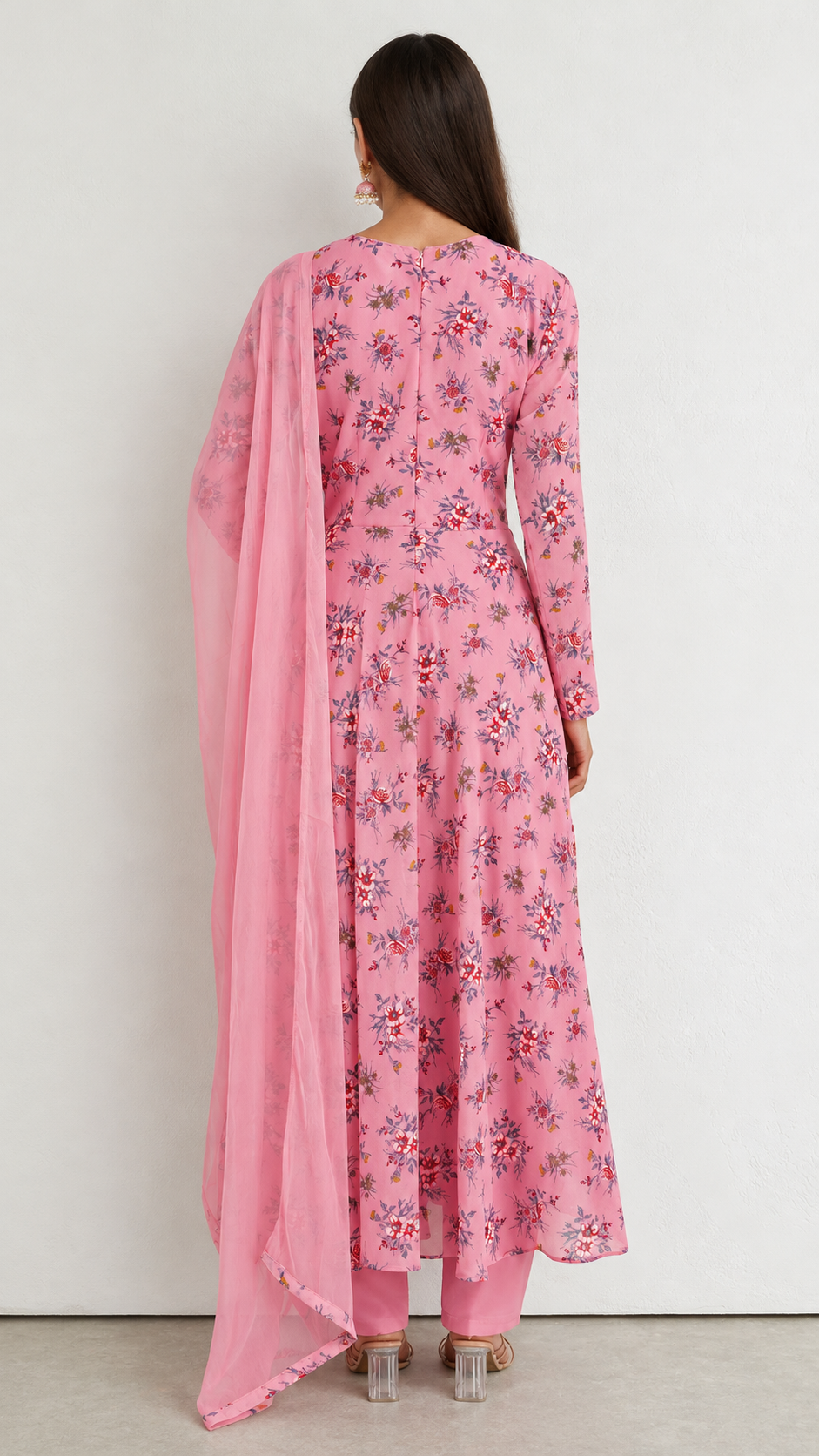 A woman shown from the back wearing a pink floral anarkali kurta with matching pants and a sheer pink dupatta, set against a plain white wall.