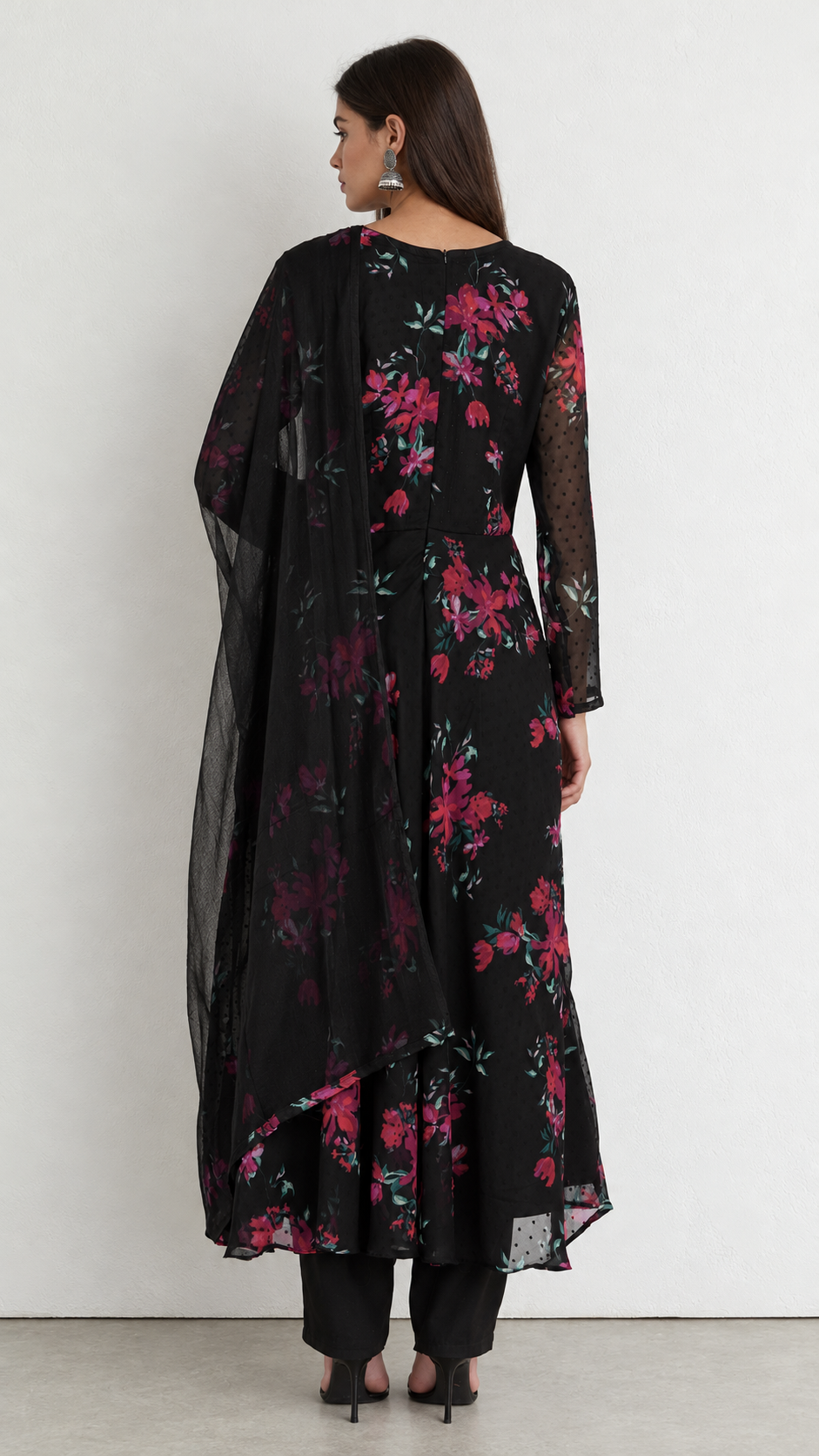 A woman shown from the back wearing a black long kurta with a vibrant pink and red floral print, paired with black pants and a sheer black dupatta, set against a plain white wall.