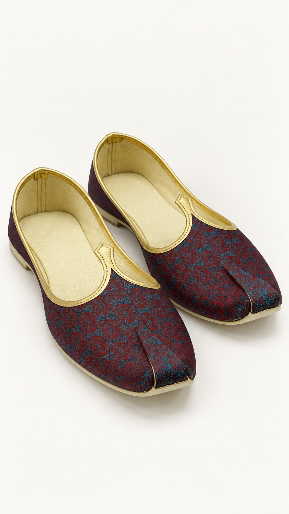 A pair of traditional Indian groom's shoes, known as Khussa, featuring a deep maroon and blue patterned brocade fabric upper with gold trim and a cream-colored footbed.