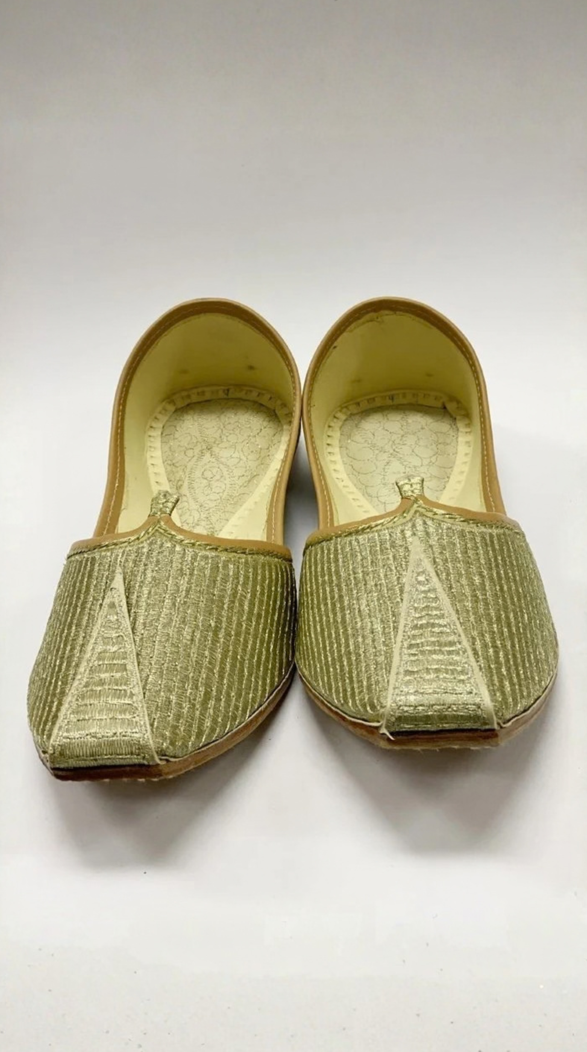 A pair of traditional slip-on flat shoes with a textured olive green woven fabric upper and a light beige interior, shown against a plain light gray background.