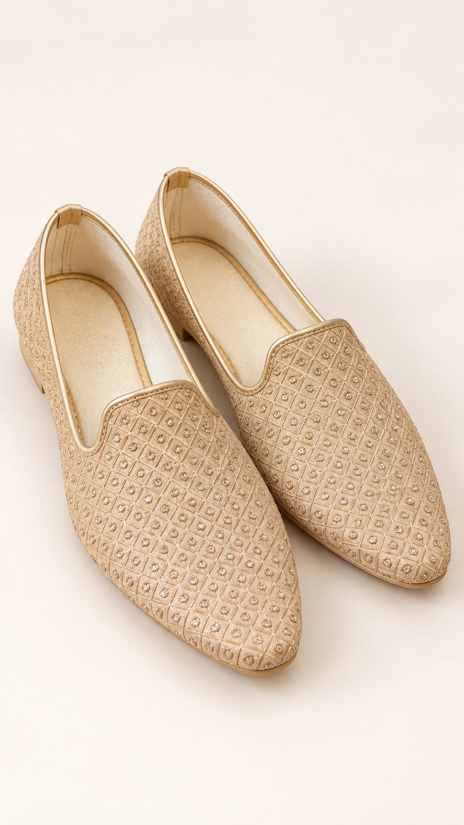 A pair of gold slip-on loafers with a textured geometric woven pattern, displayed on a light cream background.