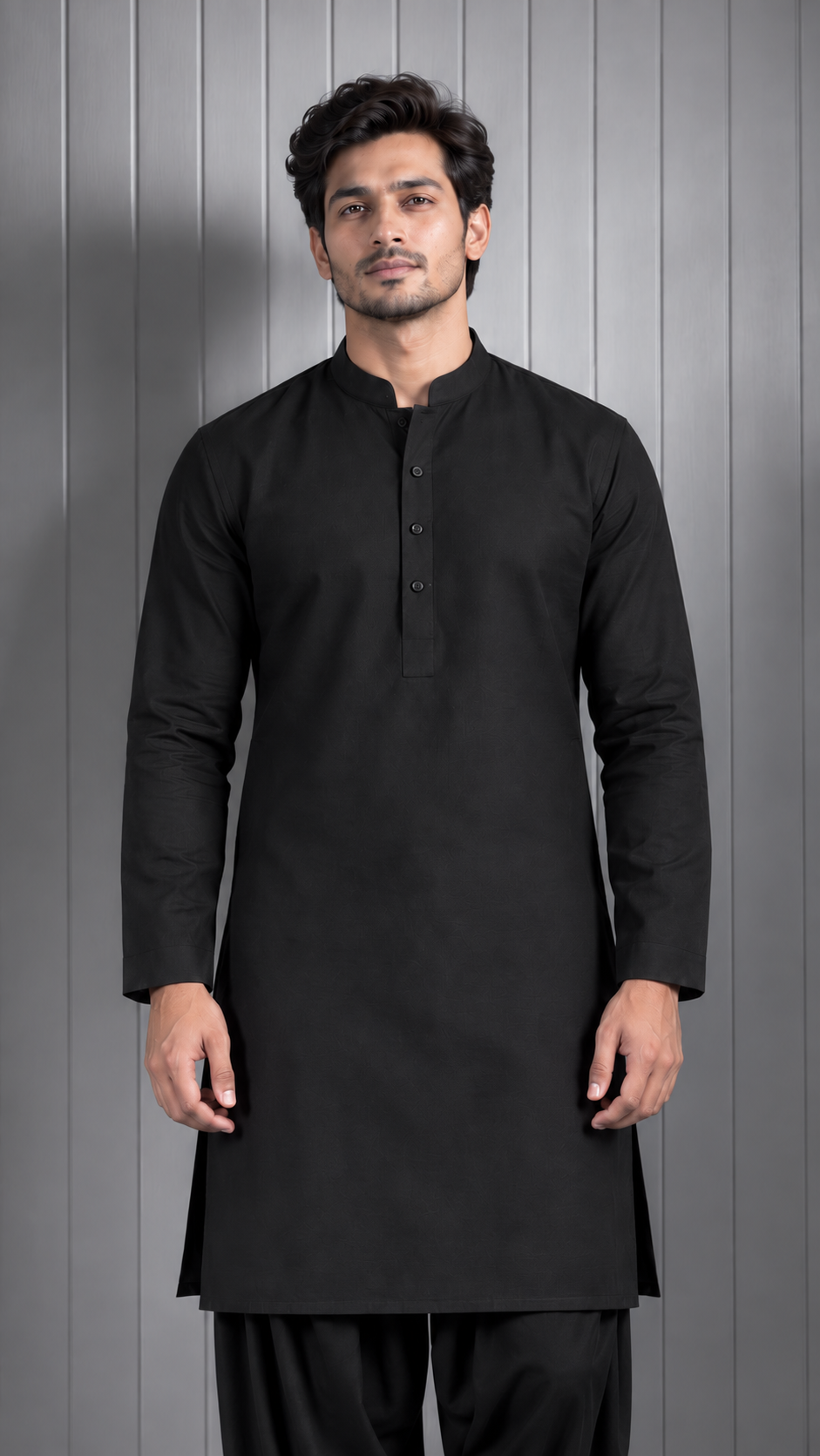 A man wearing a black long-sleeve kurta with a mandarin collar and three-button placket, paired with black trousers, standing against a gray paneled background.