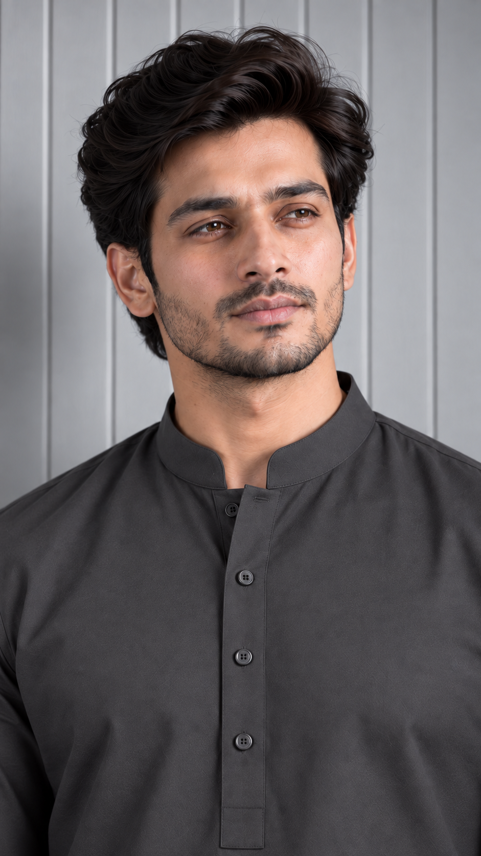 A man wearing a dark charcoal gray mandarin collar kurta, shown from the chest up against a light gray paneled background.