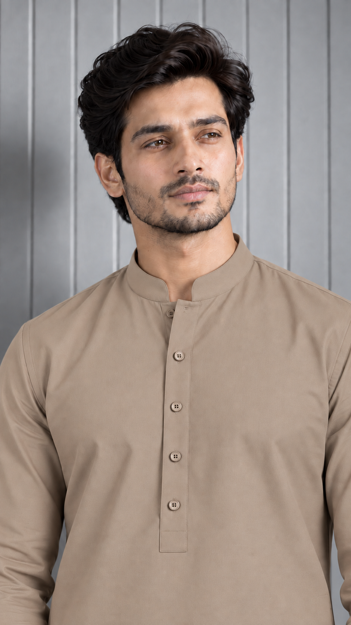 A man wearing a beige long-sleeve kurta with a mandarin collar and a buttoned placket, standing against a gray paneled background.