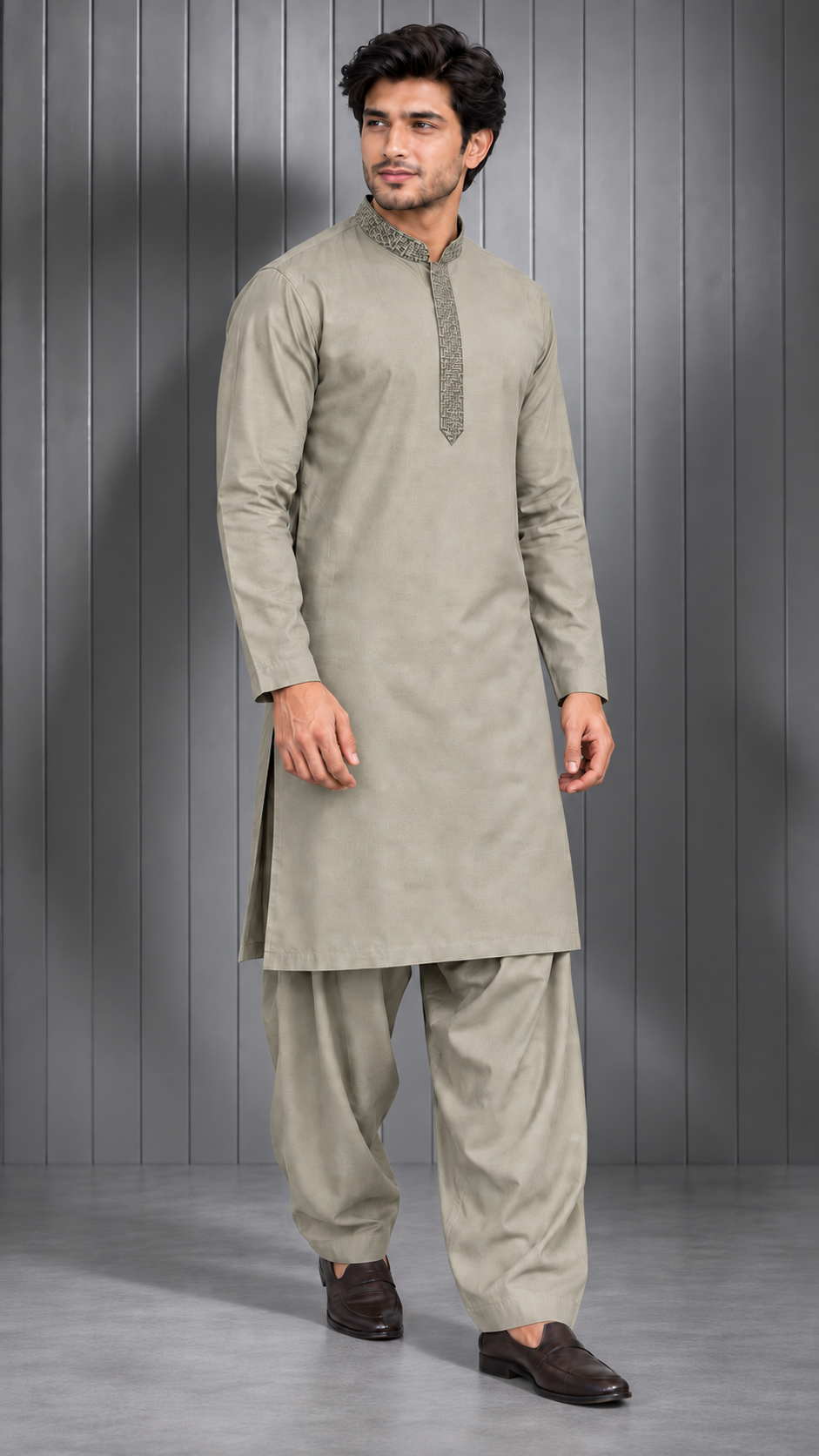 A man modeling a light beige/khaki-colored traditional Indian outfit consisting of a long-sleeve kurta with a decorative collar and matching loose-fitting trousers, standing against a gray paneled studio background.