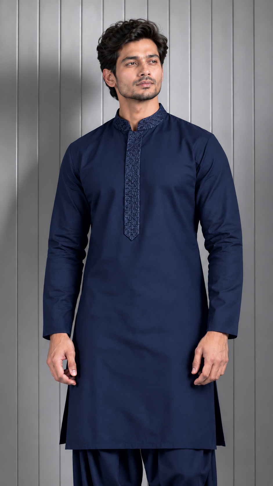 A man wearing a dark navy blue kurta with a patterned mandarin collar and chest placket, paired with matching navy trousers, standing against a gray paneled background.