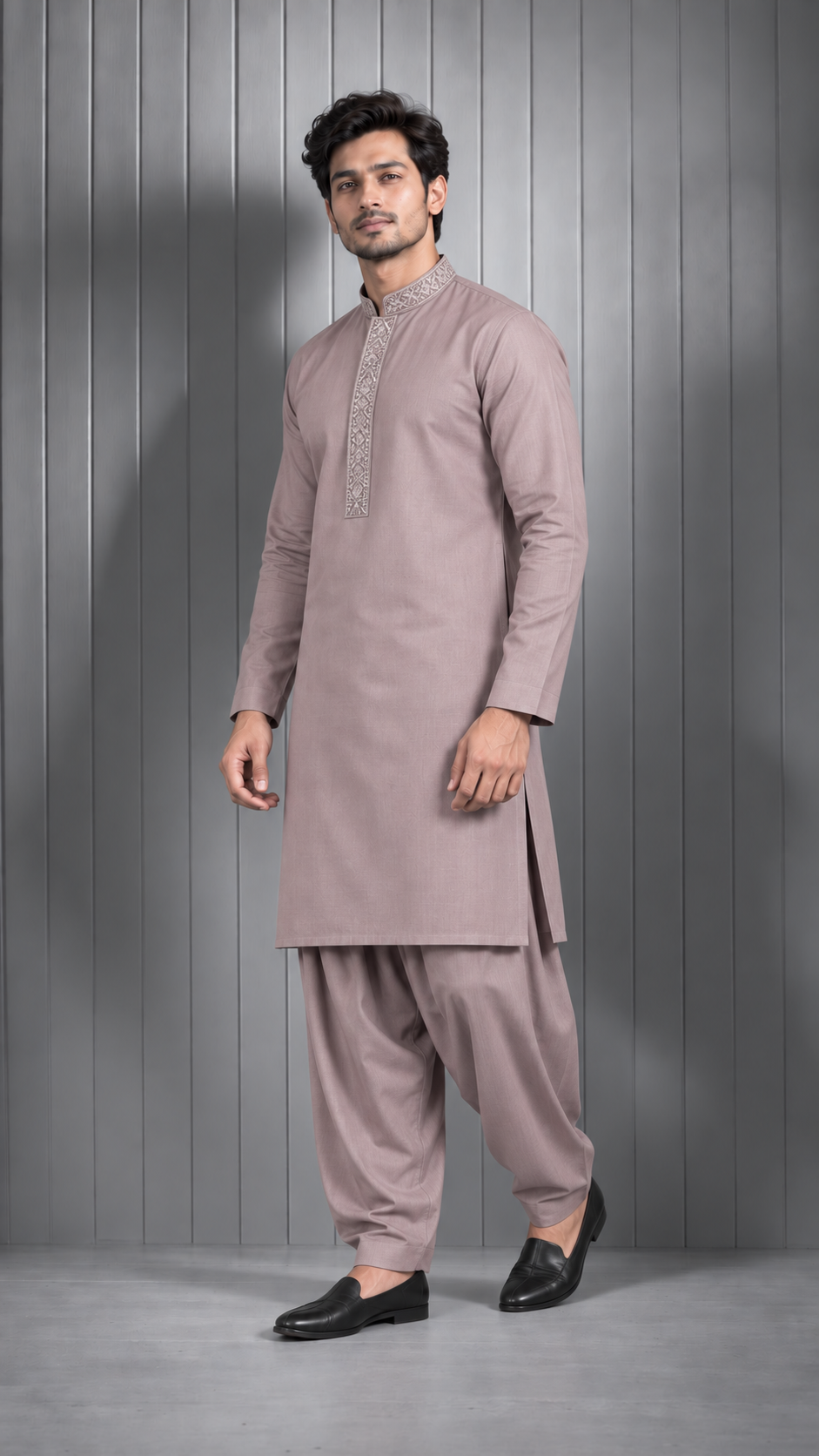 A man modeling a traditional Indian outfit consisting of a dusty rose kurta with silver embroidery on the chest and matching wide-leg pants, standing against a gray paneled wall.