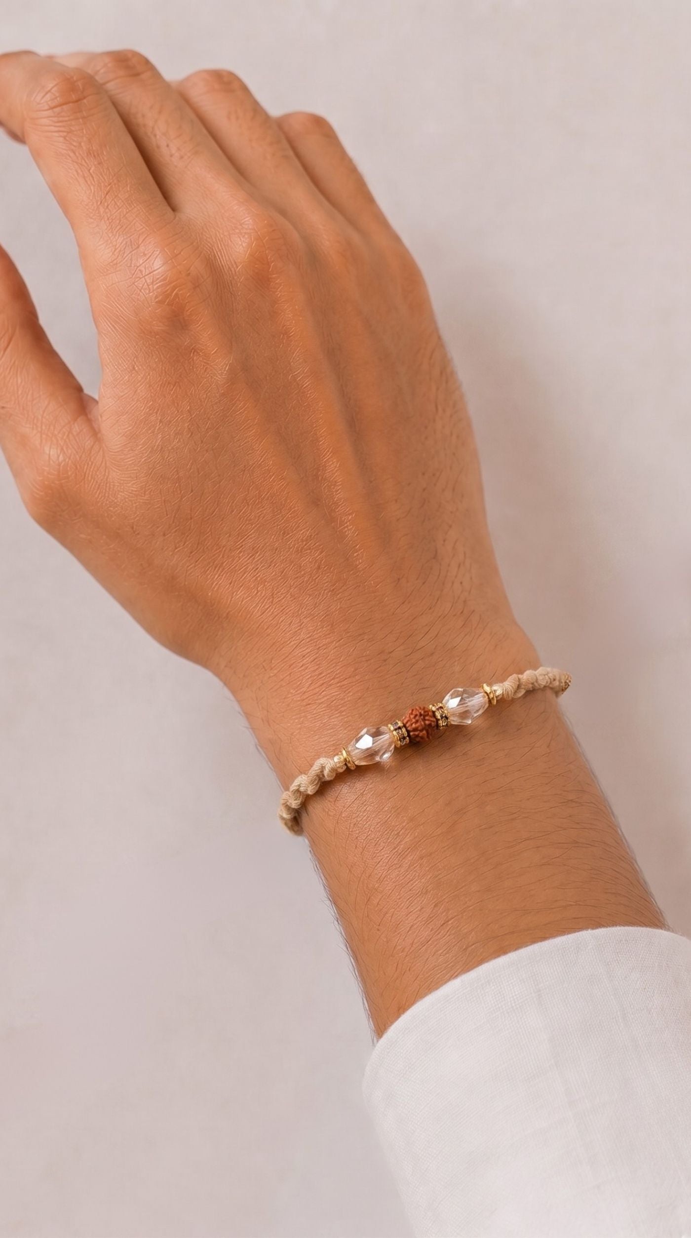 Rudraksha rakhi with clear crystal beads, gold-tone spacers, and beige braided thread worn on a man's wrist – Diya Online