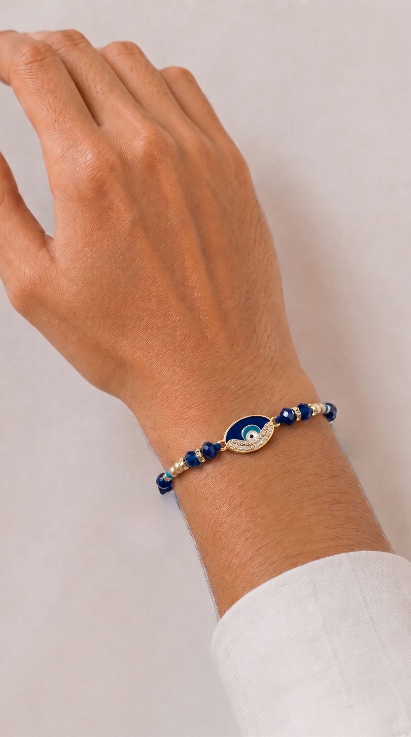 Navy evil eye rakhi bracelet with crystal detailing, faceted blue beads, pearl accents, and adjustable navy thread worn on a man's wrist – Diya Online
