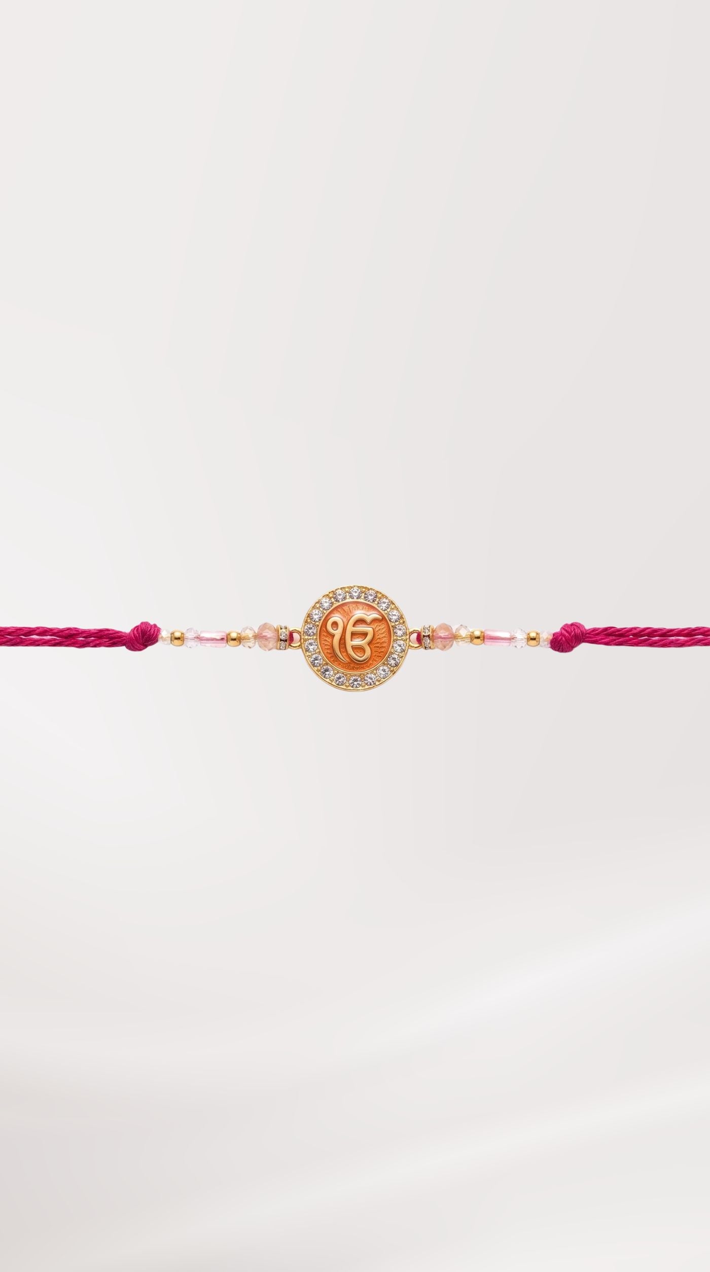 Ek Onkar rakhi bracelet with crystal-studded gold-tone Ek Onkar charm, pink pearl beads, white seed beads, and adjustable pink thread worn on a man's wrist – Diya Online