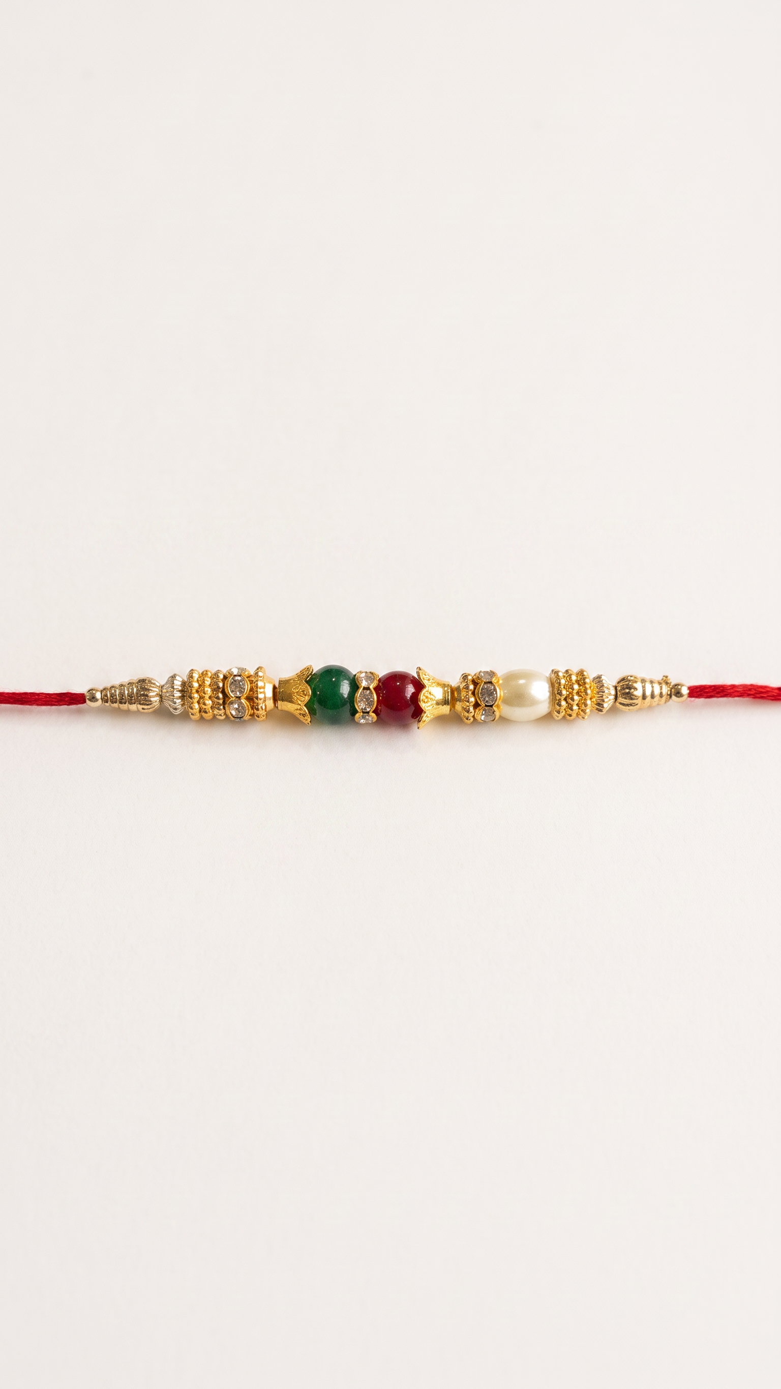 Gold-tone Rakhi with red, green and pearl beads worn on a young Indian man’s wrist – Diya Online