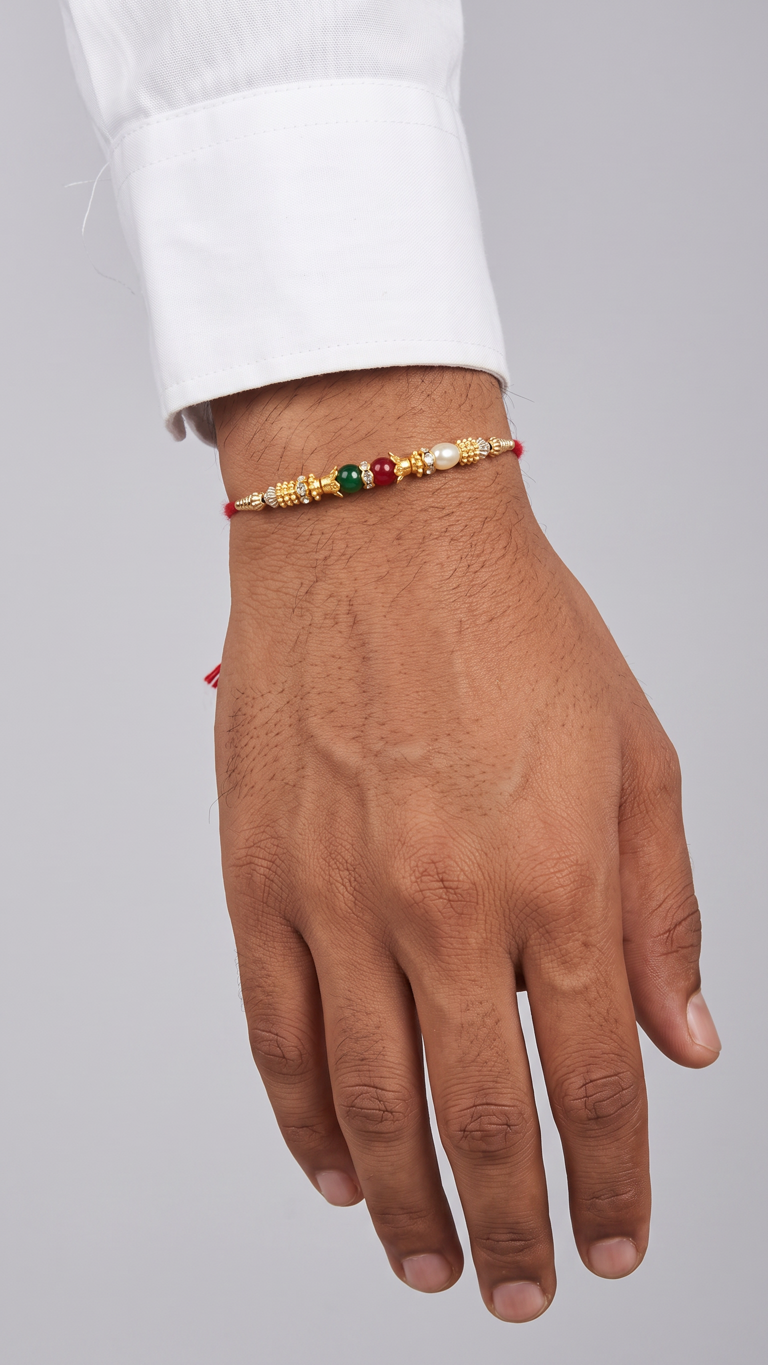 Gold-tone Rakhi with red, green and pearl beads worn on a young Indian man’s wrist – Diya Online