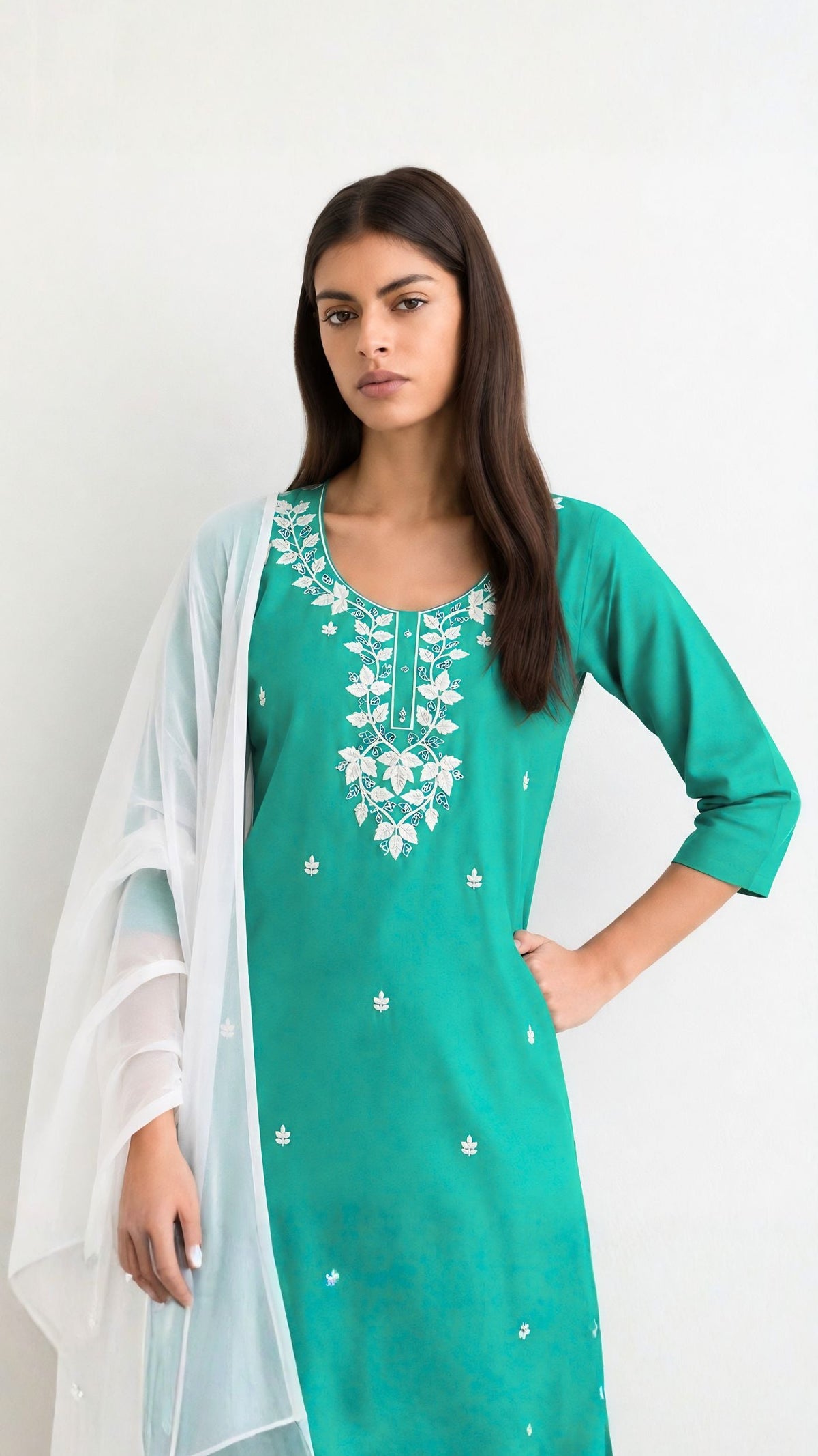 A woman modeling a teal green kurta with white floral embroidery on the neckline and scattered small motifs, paired with a sheer white dupatta, against a plain white background.