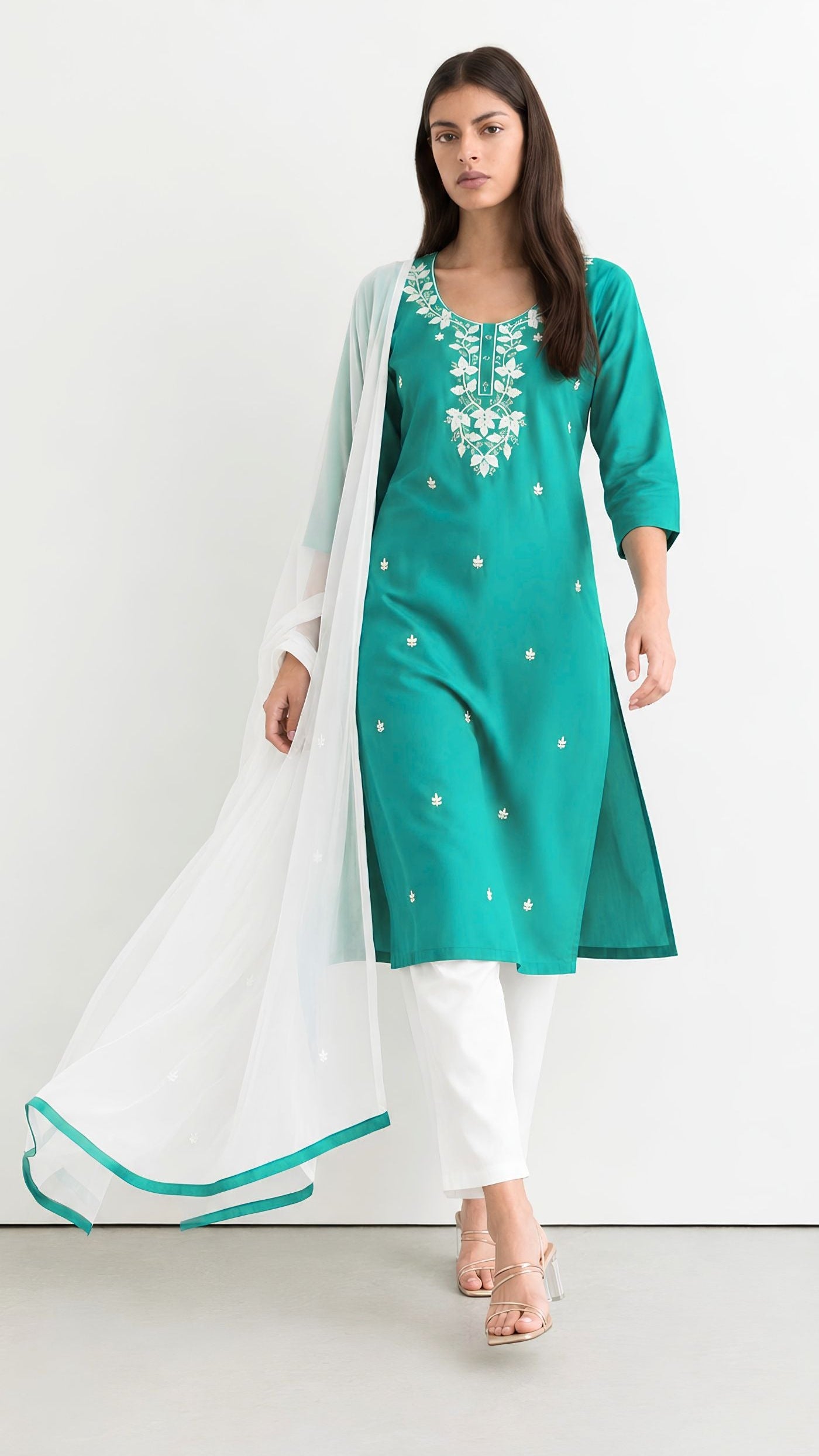 A woman modeling a teal green kurta with white embroidery, paired with white pants and a sheer white dupatta with a teal border, set against a plain white studio background.
