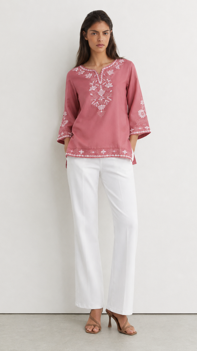 Young woman wearing a dusty rose embroidered kurta top with white floral threadwork, three-quarter sleeves and white flared trousers.