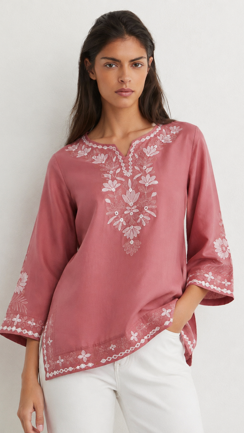 Young woman wearing a dusty rose embroidered kurta top with white floral threadwork, three-quarter sleeves and white flared trousers.