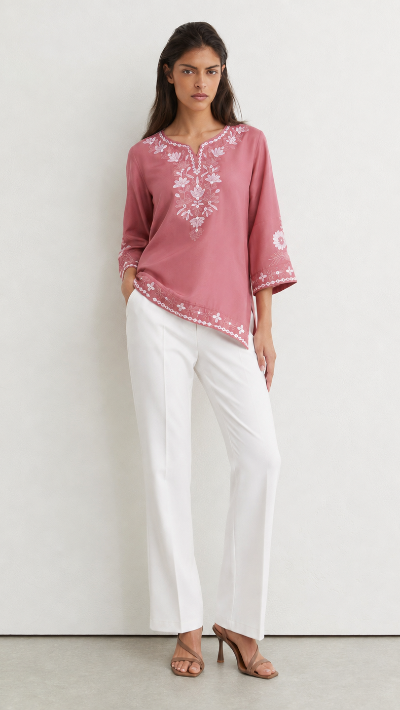 Young woman wearing a dusty rose embroidered kurta top with white floral threadwork, three-quarter sleeves and white flared trousers.