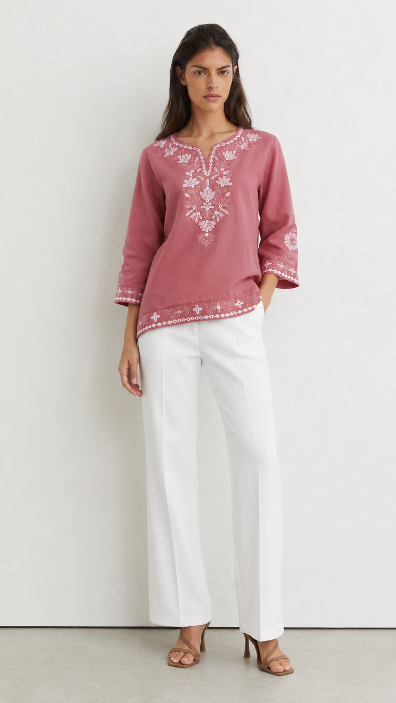Young woman wearing a dusty rose embroidered kurta top with white floral threadwork, three-quarter sleeves and white flared trousers.