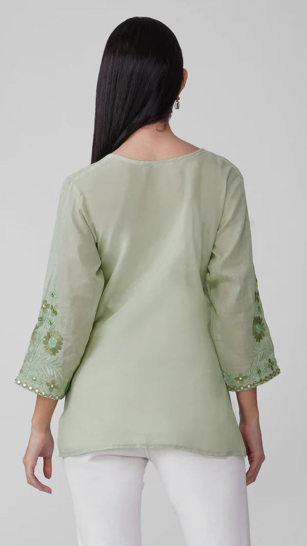 Young woman wearing a sage green embroidered kurta top with tonal floral threadwork, three-quarter sleeves and white trousers.