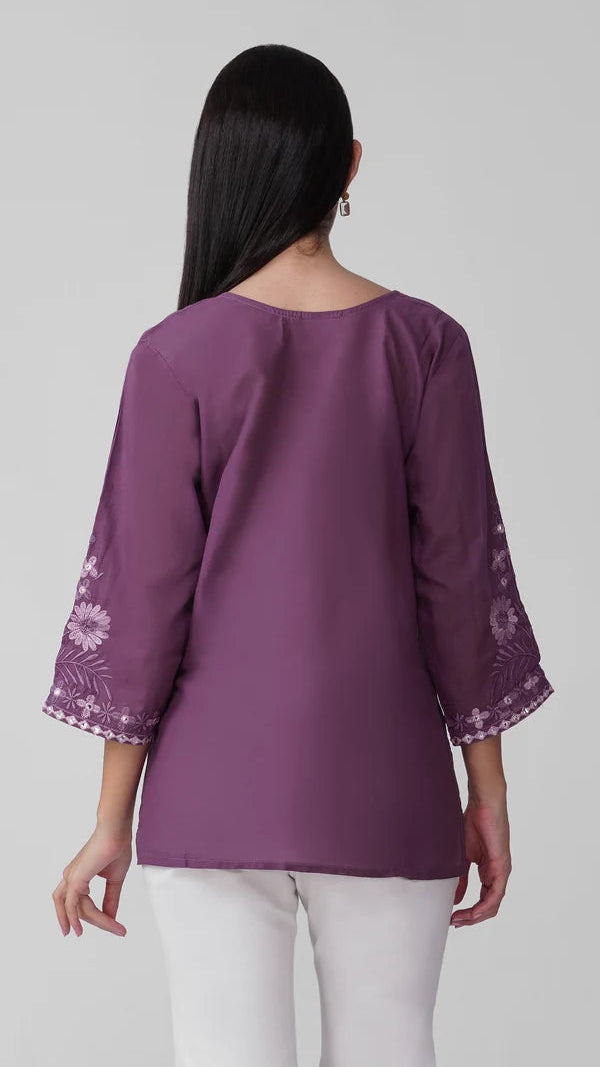 Young woman wearing a purple embroidered kurta top with tonal floral threadwork, three-quarter sleeves and white trousers.