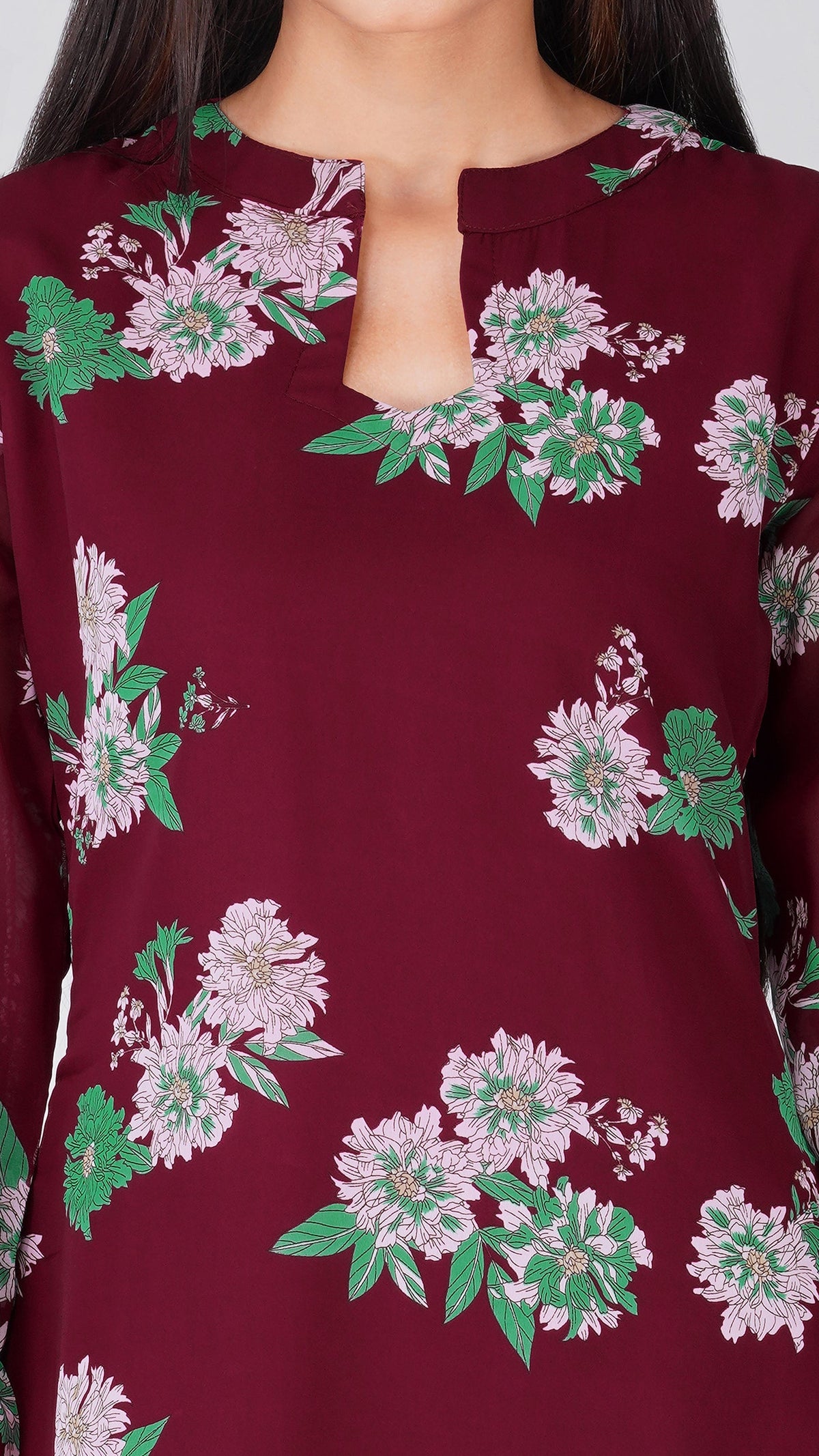 A close-up of a woman wearing a deep maroon long-sleeve top with a floral print of light pink flowers and green leaves.