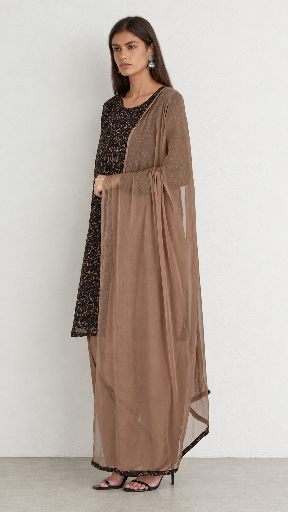 A woman modeling a traditional outfit featuring a brown sheer dupatta draped over a black embroidered kurta and matching brown trousers, set against a plain light gray studio background.