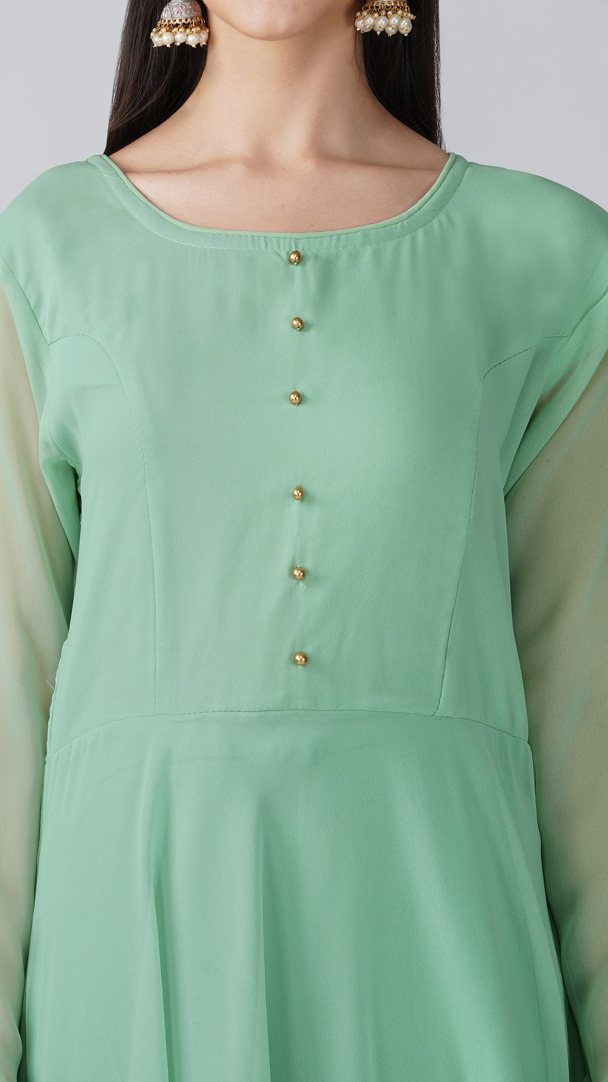 A close-up of a model wearing a mint green long-sleeve tunic or kurta with a scoop neckline and a vertical row of small gold buttons down the front.