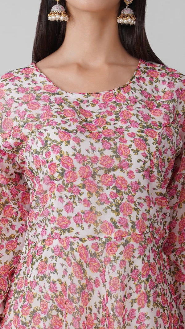 A close-up of a woman wearing a long-sleeve kurta with a pink and green floral print on a white base, paired with gold-toned jhumka earrings.