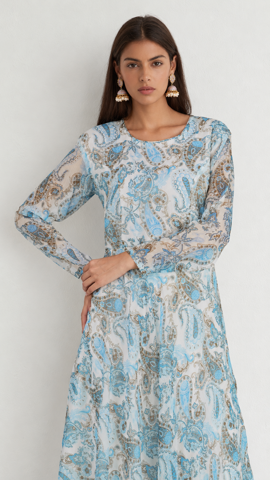 A woman modeling a long-sleeve midi dress with a light blue, beige, and white paisley pattern against a plain light gray background.