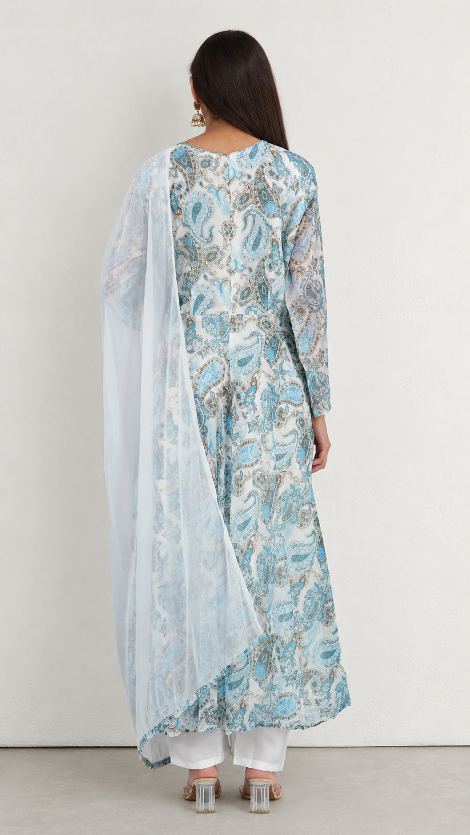 A woman shown from the back wearing a light blue and white printed kurta with a matching sheer dupatta and white pants, standing against a plain off-white wall.