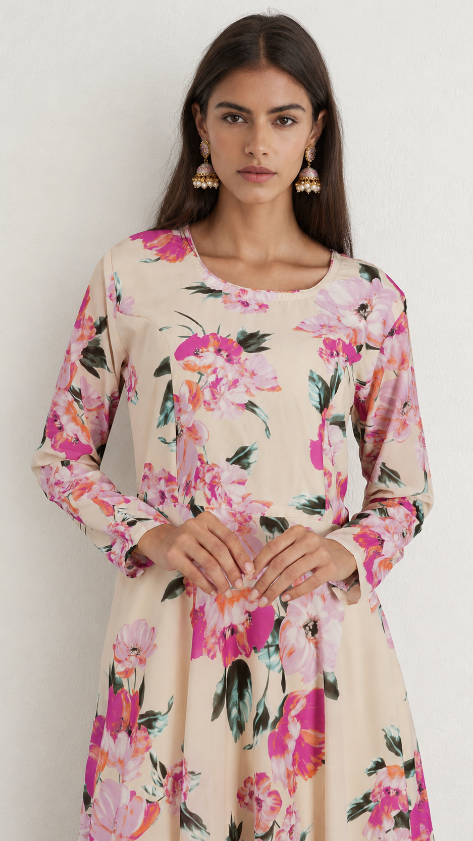 A woman wearing a long-sleeve beige tunic dress with a vibrant pink and green floral print, standing against a plain off-white background.