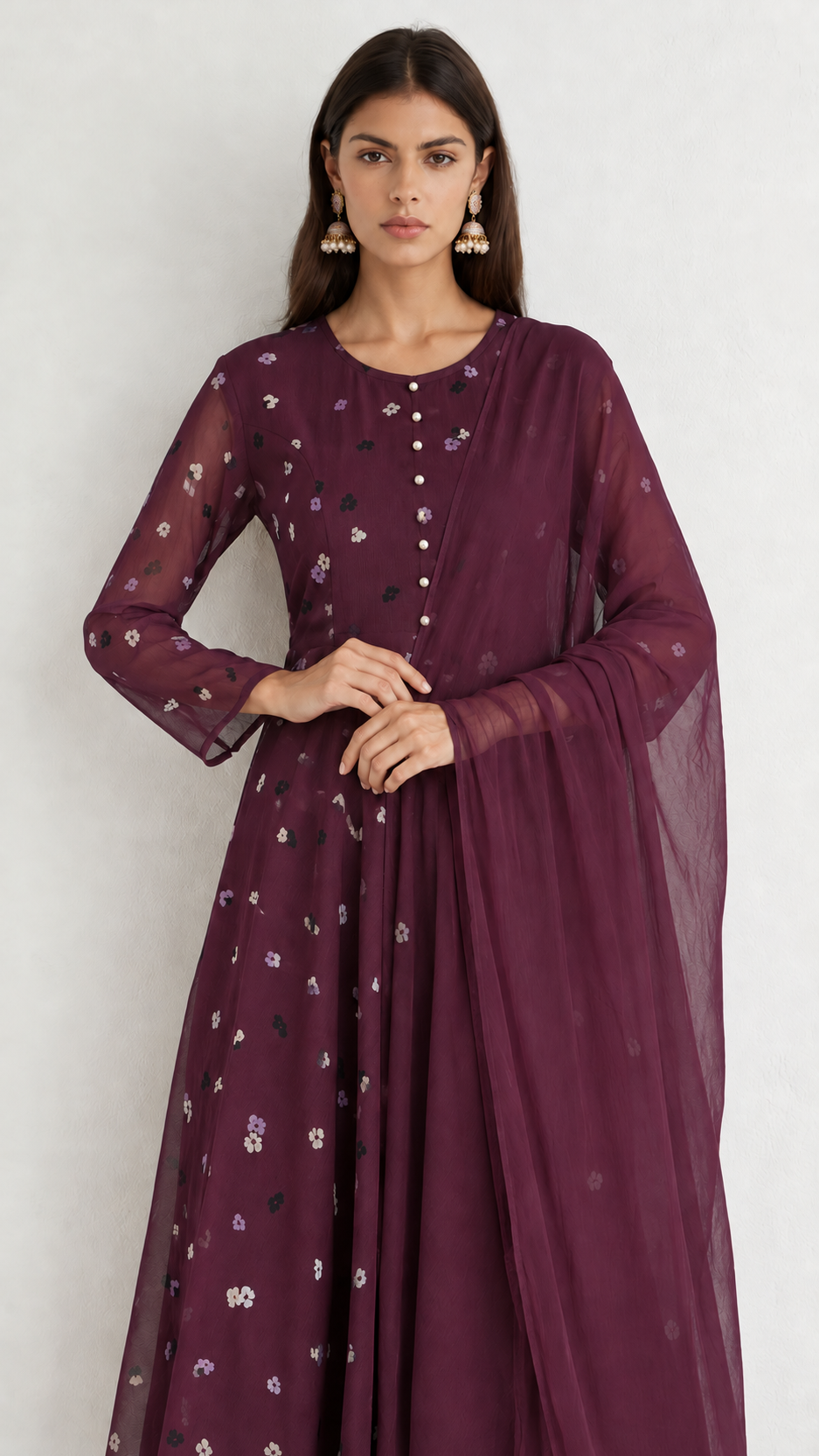A woman modeling a deep plum purple traditional kurta set with matching sheer dupatta. The kurta features a round neckline, three-quarter sleeves, and delicate white floral embroidery scattered across the fabric.